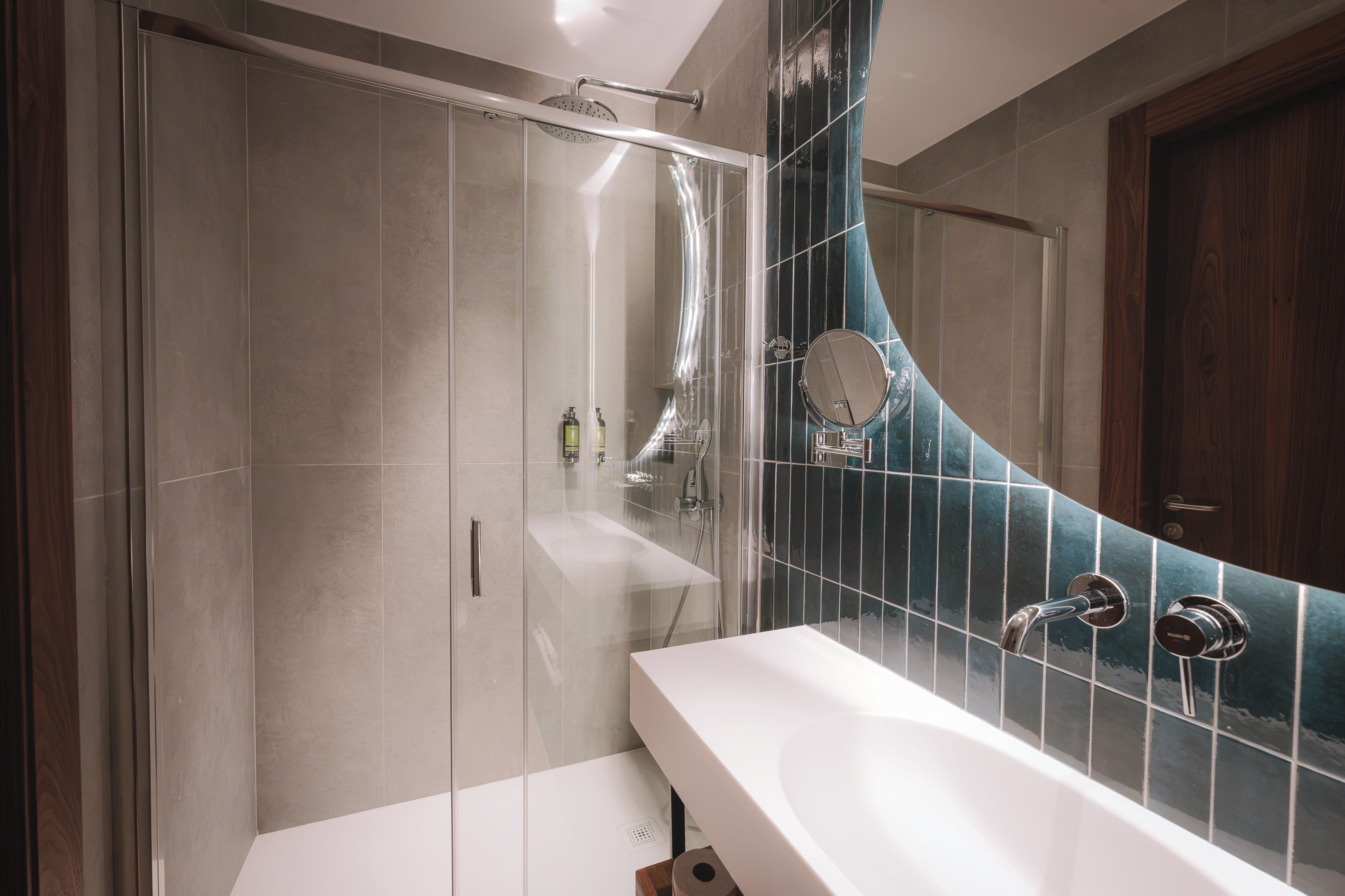 A modern bathroom with a glass shower enclosure, a white sink, and a mirror with a curved backsplash.