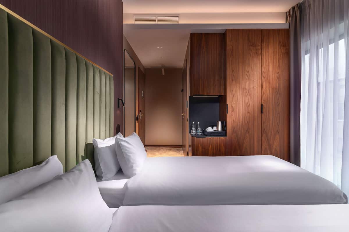 A hotel room with two beds, a wooden wardrobe, and a small table with a coffee maker.