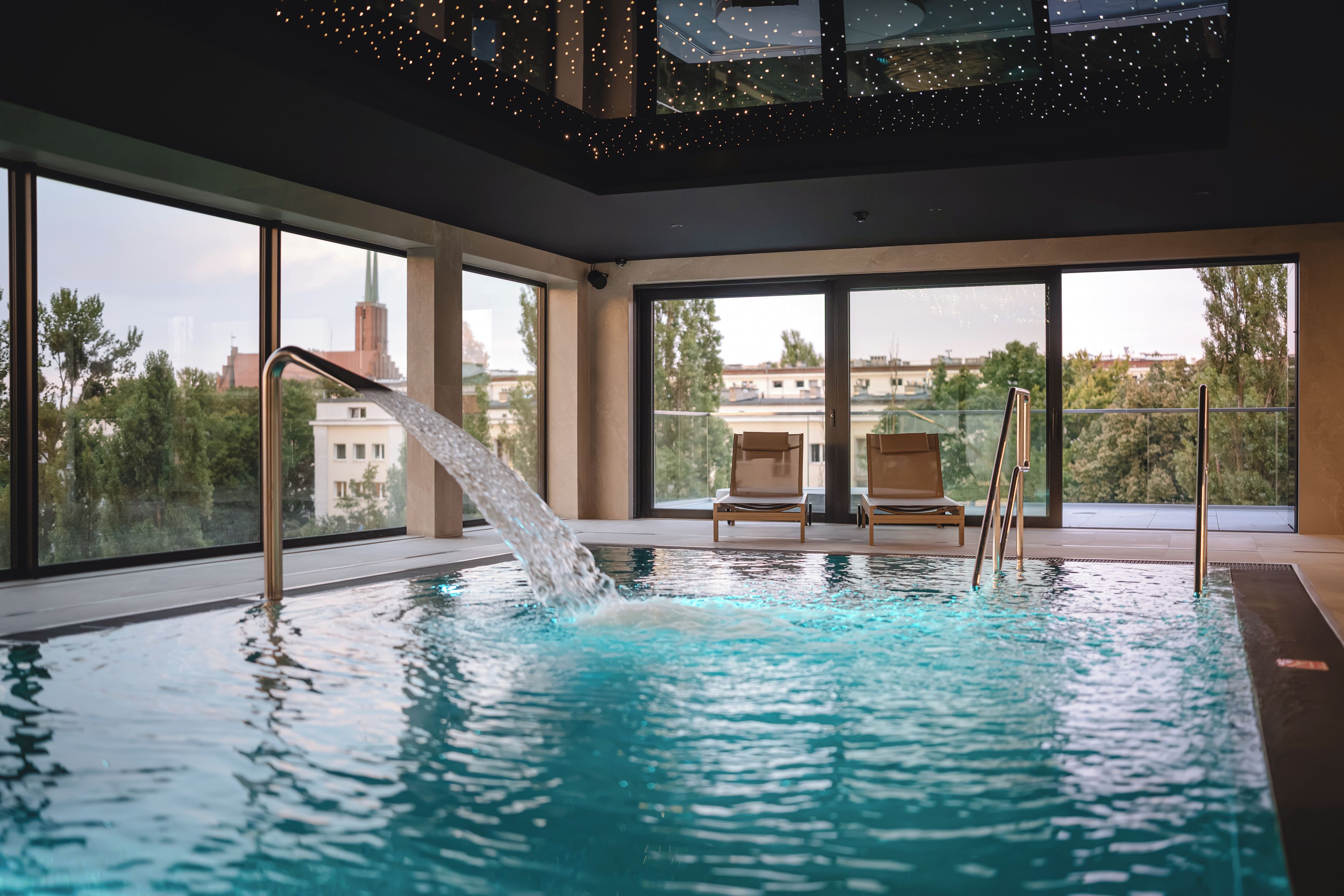 Una piscina interior con agua cristalina, una fuente de agua y sillas de descanso.