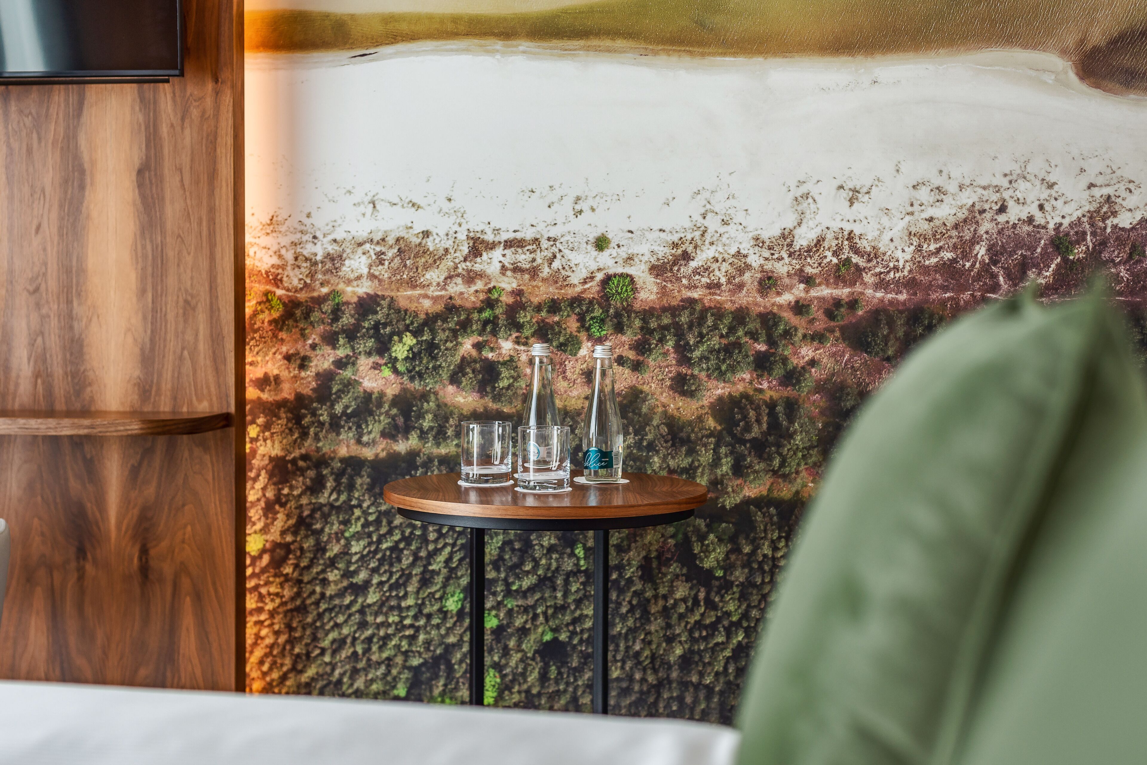 A room with a wooden cabinet, a round table with three glasses and a bottle, and a textured wall with a green pillow visible.