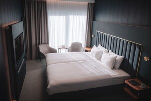 Una habitación de hotel con una cama grande, dos sillas, una mesita y un televisor.