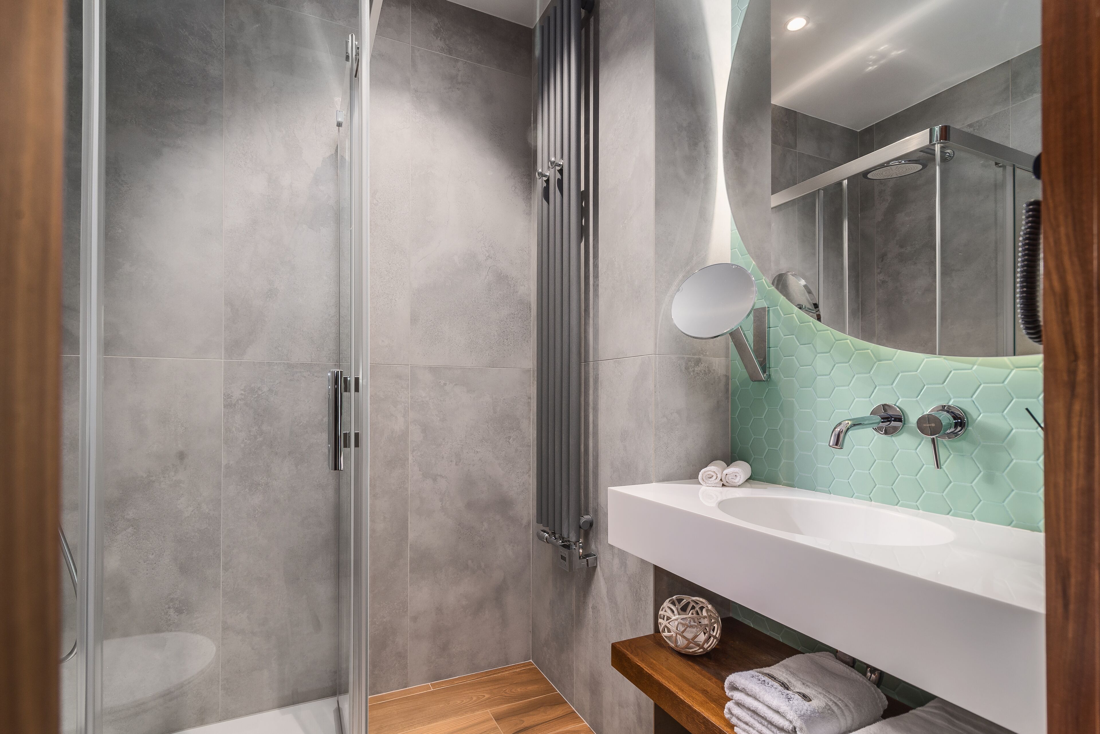 Un baño moderno con ducha de vidrio, lavabo blanco y espejo con zócalo de azulejos hexagonales.