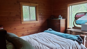 Una habitación tipo cabaña de madera con una cama, un aparador y un ventanal.