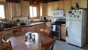 Una cocina con armarios de madera, microondas, estufa y refrigerador. Hay una mesa de comedor con sillas.