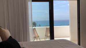 A bedroom with a large bed, a view of the ocean, and a balcony with chairs.