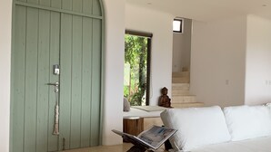 A modern living room with a green door, a white sofa, and a wooden coffee table with a newspaper.