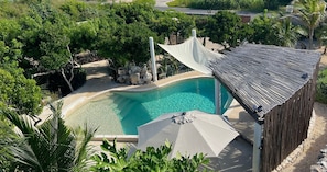 A swimming pool with a white canopy and a wooden fence, surrounded by lush greenery.