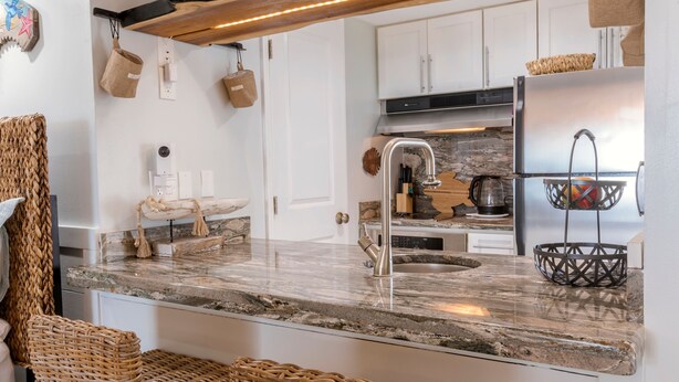 A modern kitchen with white cabinets, a marble countertop, a stainless steel sink, and a built-in oven. - Stunning Ocean Views STEPS from the Beach with Pool! Fabulous 4th Floor Studio! (New Smyrna Beach)