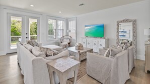 A spacious living room with a large TV, comfortable seating, and a view of the outdoors. - 4 Bedroom Gorgeous Beachy Home - Resort Pool - 6 Seater Golf Cart (Santa Rosa Beach)