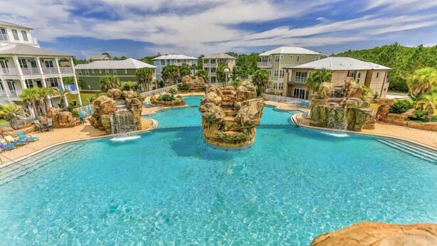 A large outdoor swimming pool with rock formations and lounge chairs. - 4 Bedroom Gorgeous Beachy Home - Resort Pool - 6 Seater Golf Cart (Santa Rosa Beach)