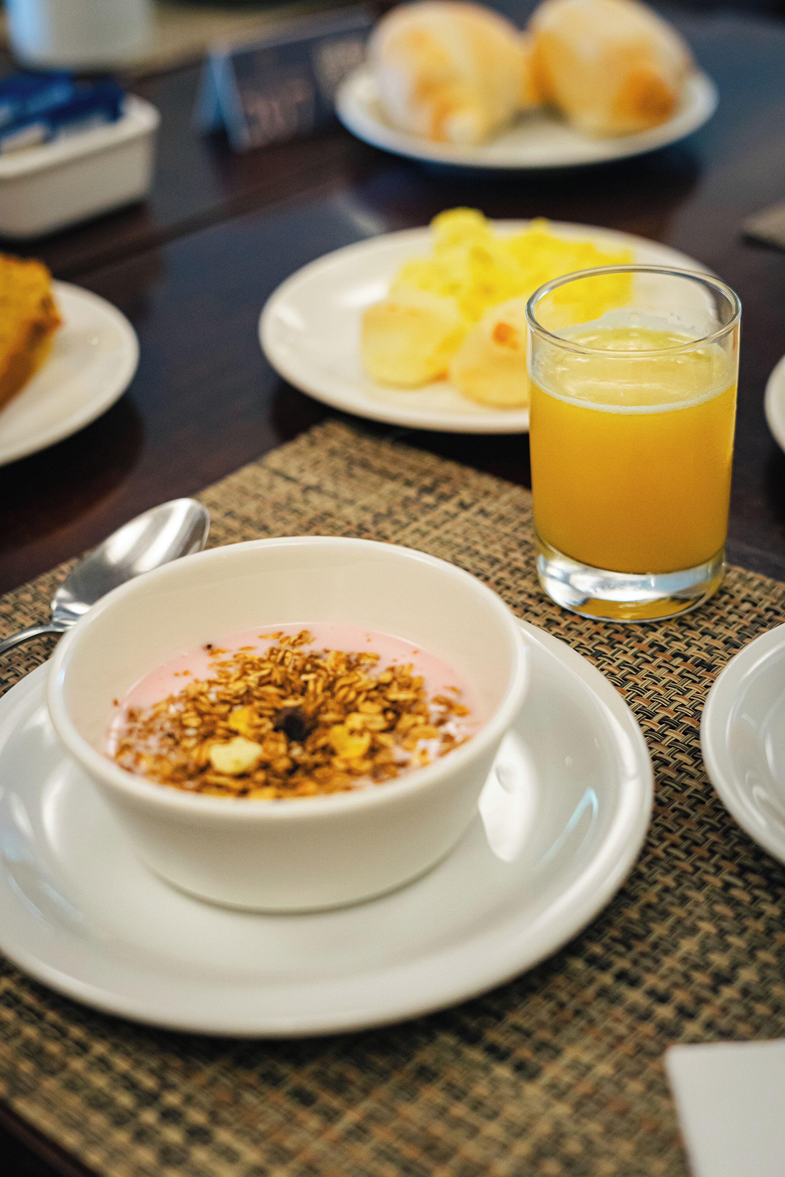 Uma mesa de café da manhã com uma tigela de iogurte coberta de granola e um copo de suco de laranja.
