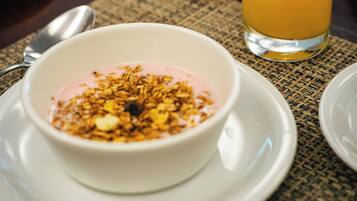 Uma mesa de café da manhã com uma tigela de iogurte coberta de granola e um copo de suco de laranja.