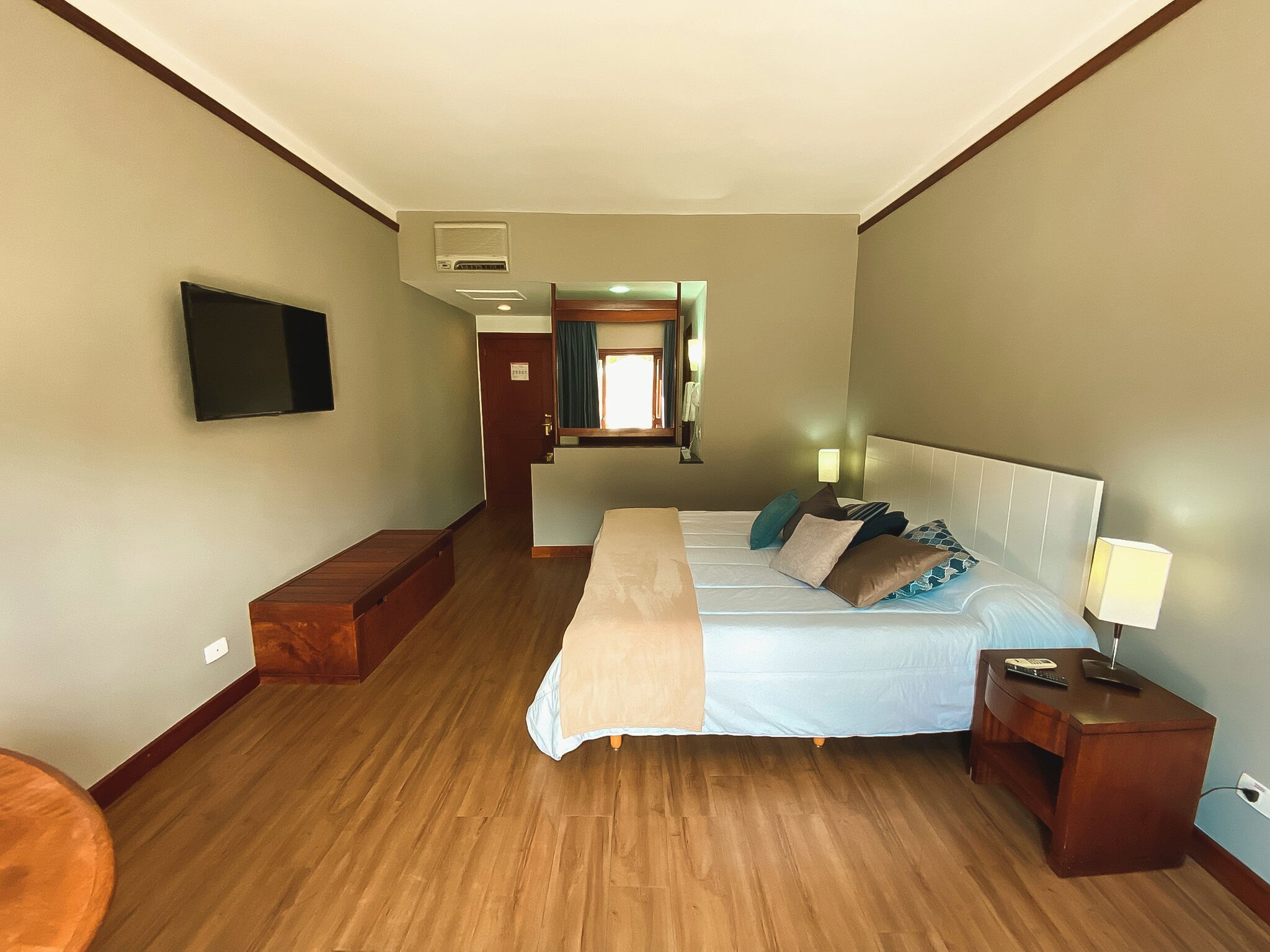 A hotel room with a bed, bedside table, lamp, and a television on the wall.