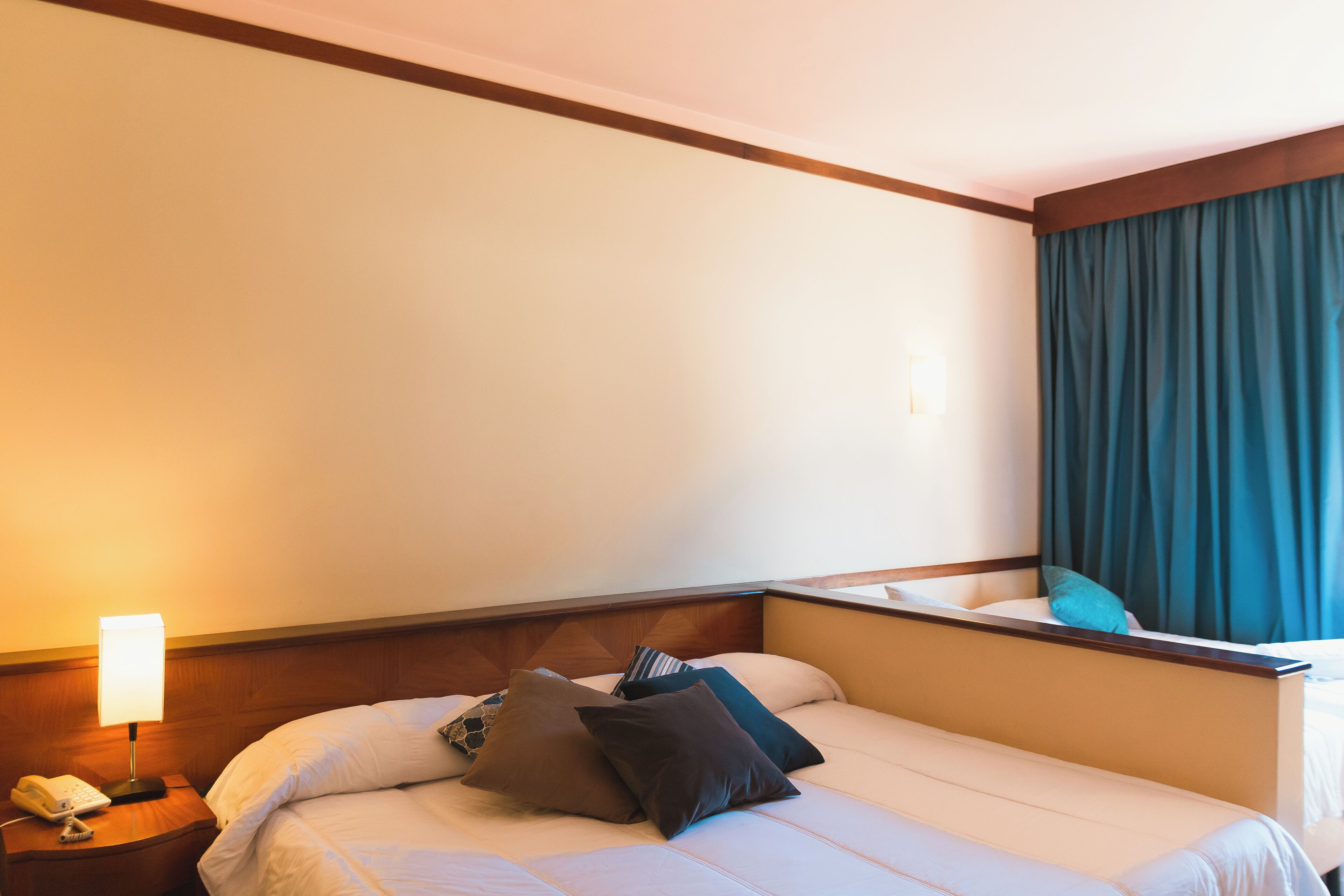 Una habitación de hotel con una cama, una mesita de noche con lámpara y una ventana con cortinas.