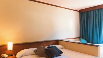 Una habitación de hotel con una cama, una mesita de noche con lámpara y una ventana con cortinas.