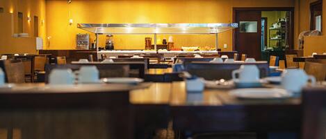 A hotel dining area with multiple tables and chairs, a buffet counter, and a coffee station.