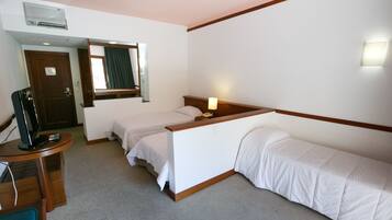 Een hotelkamer met twee bedden, een bureau met computer en telefoon, een spiegel en een raam met gordijnen.