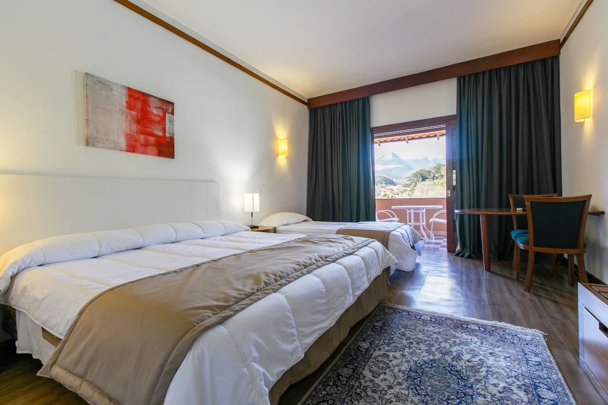 Un cuarto de hotel con dos camas, un escritorio, una silla, vista al exterior y un cuadro en la pared.