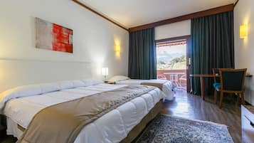 A hotel room with two beds, a desk, a chair, a view of the outdoors, and a painting on the wall.