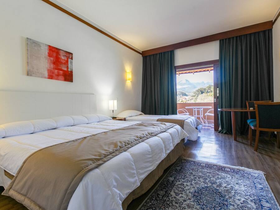 A hotel room with two beds, a desk, a chair, a view of the outdoors, and a painting on the wall.