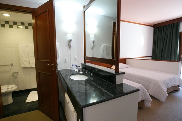 A hotel room with a bathroom, a bed, and a large mirror.