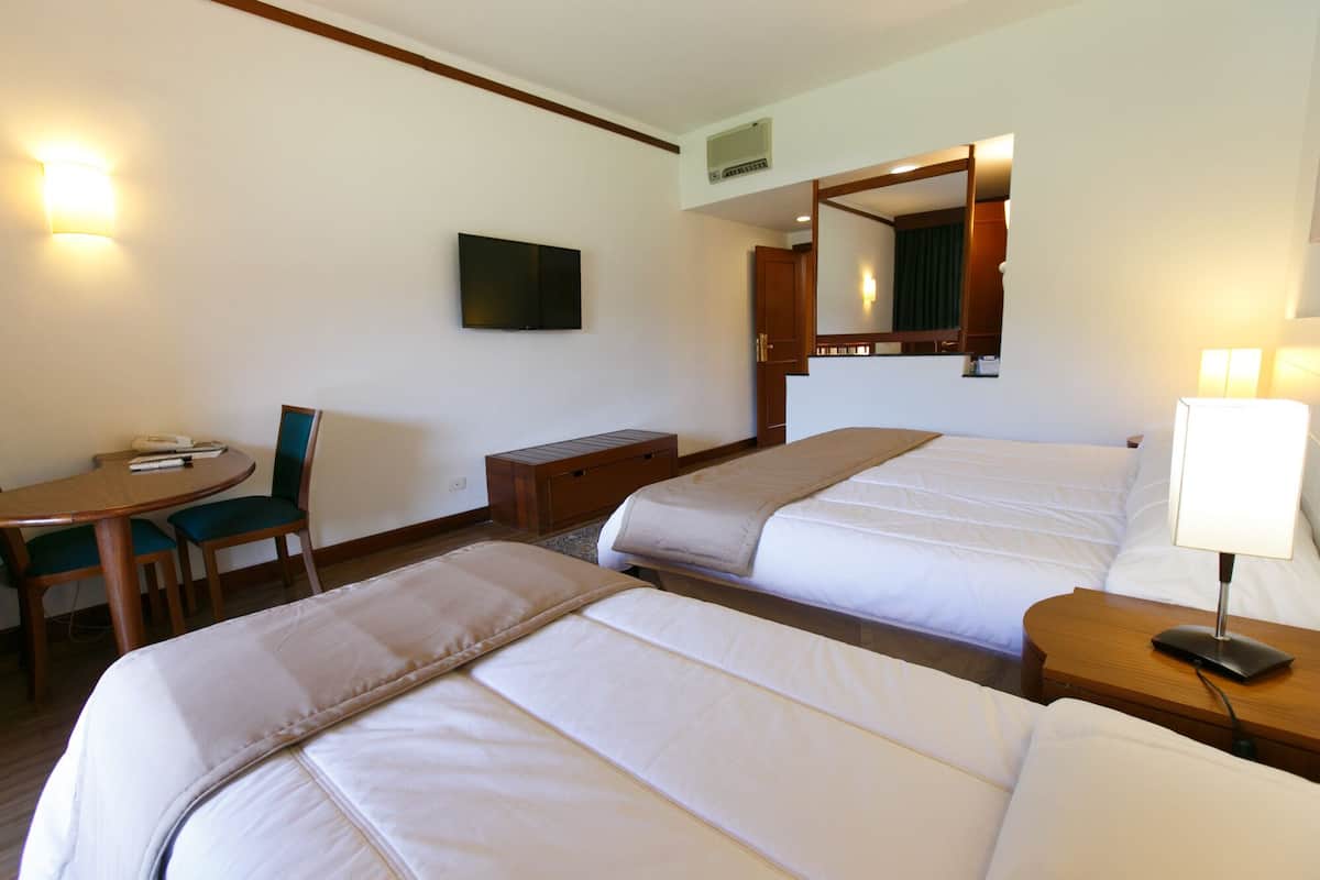 Una habitación de hotel con dos camas, un escritorio, una silla, un televisor y una lámpara.
