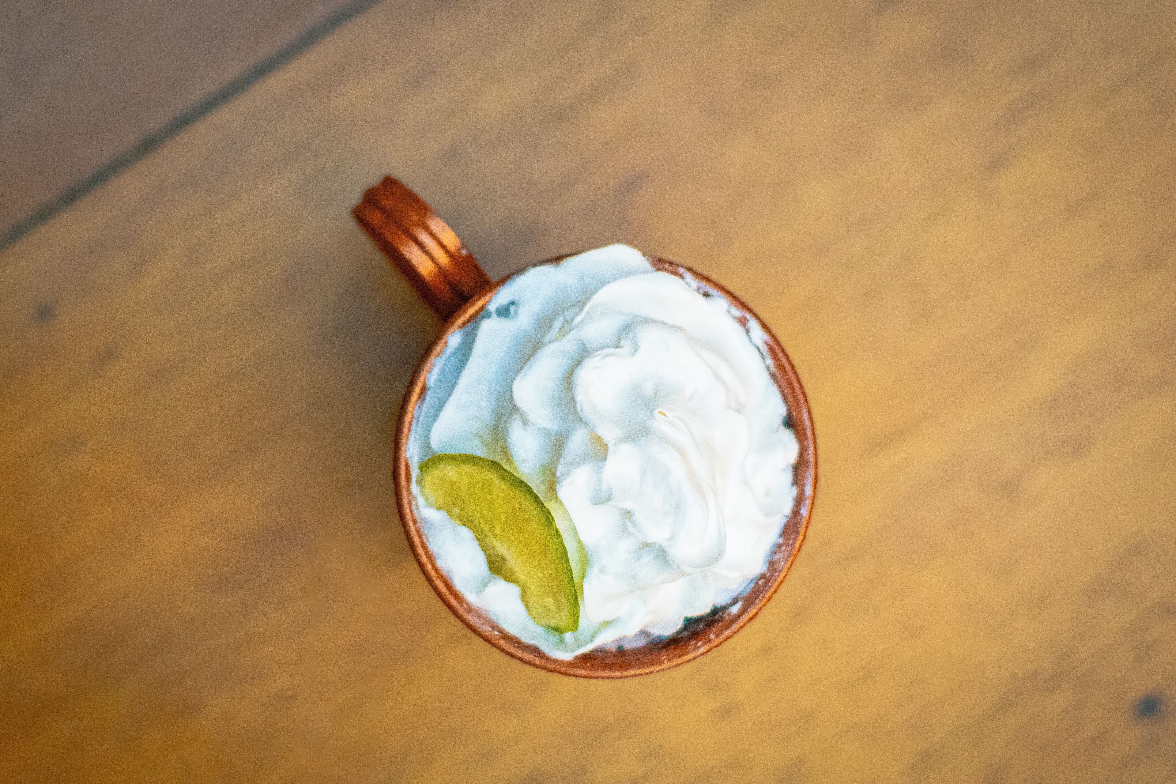 A cup with whipped cream and a lime wedge on a wooden surface.