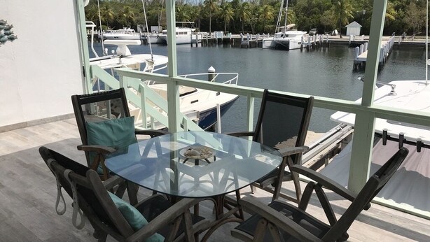 A glass-top table with chairs, a view of a marina with boats, and a building with a light green exterior. - Beautifully remodeled  “Over the water” Townhouse suite! (Berry Islands)