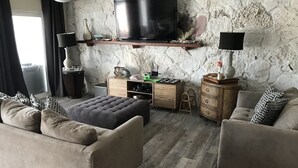 A living room with a stone wall, a flat-screen TV, a wooden cabinet, and two sofas. - Beautifully remodeled  “Over the water” Townhouse suite! (Berry Islands)