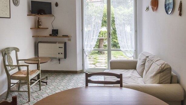 A room with a sofa, a chair, a table, a television on a shelf, and a sliding glass door to a garden. - M297 - Marcelli, three-room apartment with garden at 100 m. from the sea (Marcelli)