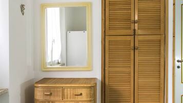 Una stanza con un'armadio in legno, uno specchio con cornice gialla e un comò in vimini.