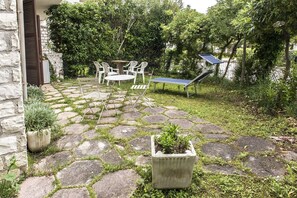 Un patio de piedra con mobiliario exterior, una mesa de ping pong y plantas en macetas.