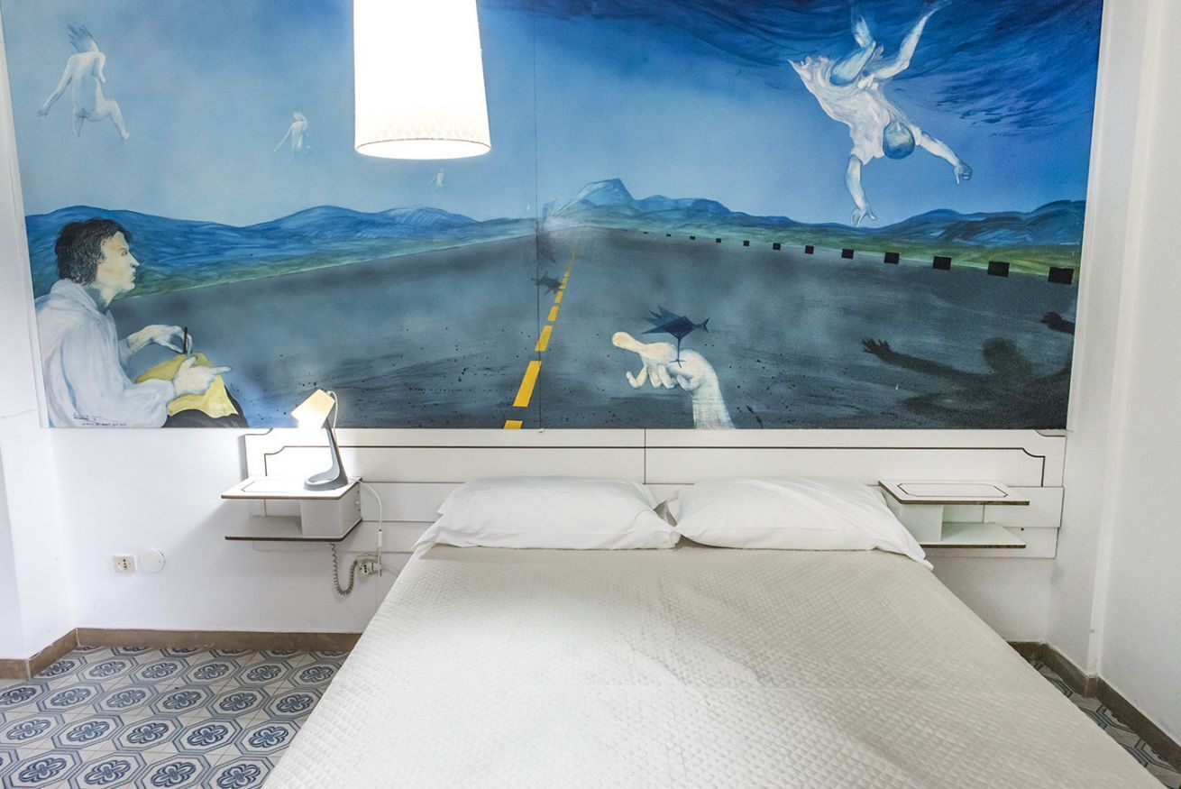 Una camera da letto con un letto, un comodino, una lampada e un affresco sulla parete.