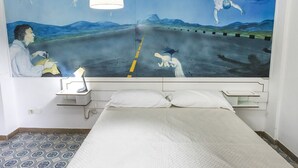 A bedroom with a bed, a nightstand, a lamp, and a wall mural. - M297 - Marcelli, three-room apartment with garden at 100 m. from the sea (Marcelli)