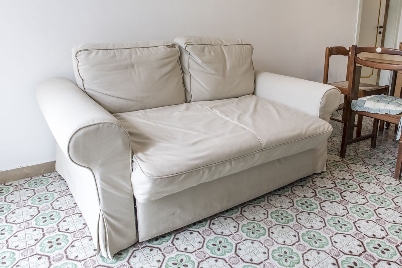 Un canapé beige, doté d’accoudoirs et d’un coussin, est placé sur des carreaux de sol à motifs.