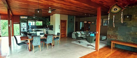 A spacious living area with a high ceiling, wooden flooring, and a kitchen in the background.