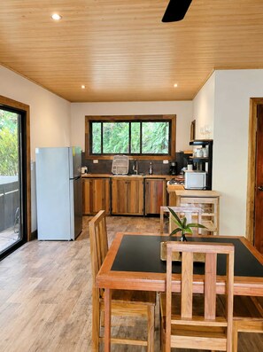 A modern kitchen with wooden cabinets, a built-in coffee machine, and a dining area with a table and chairs.