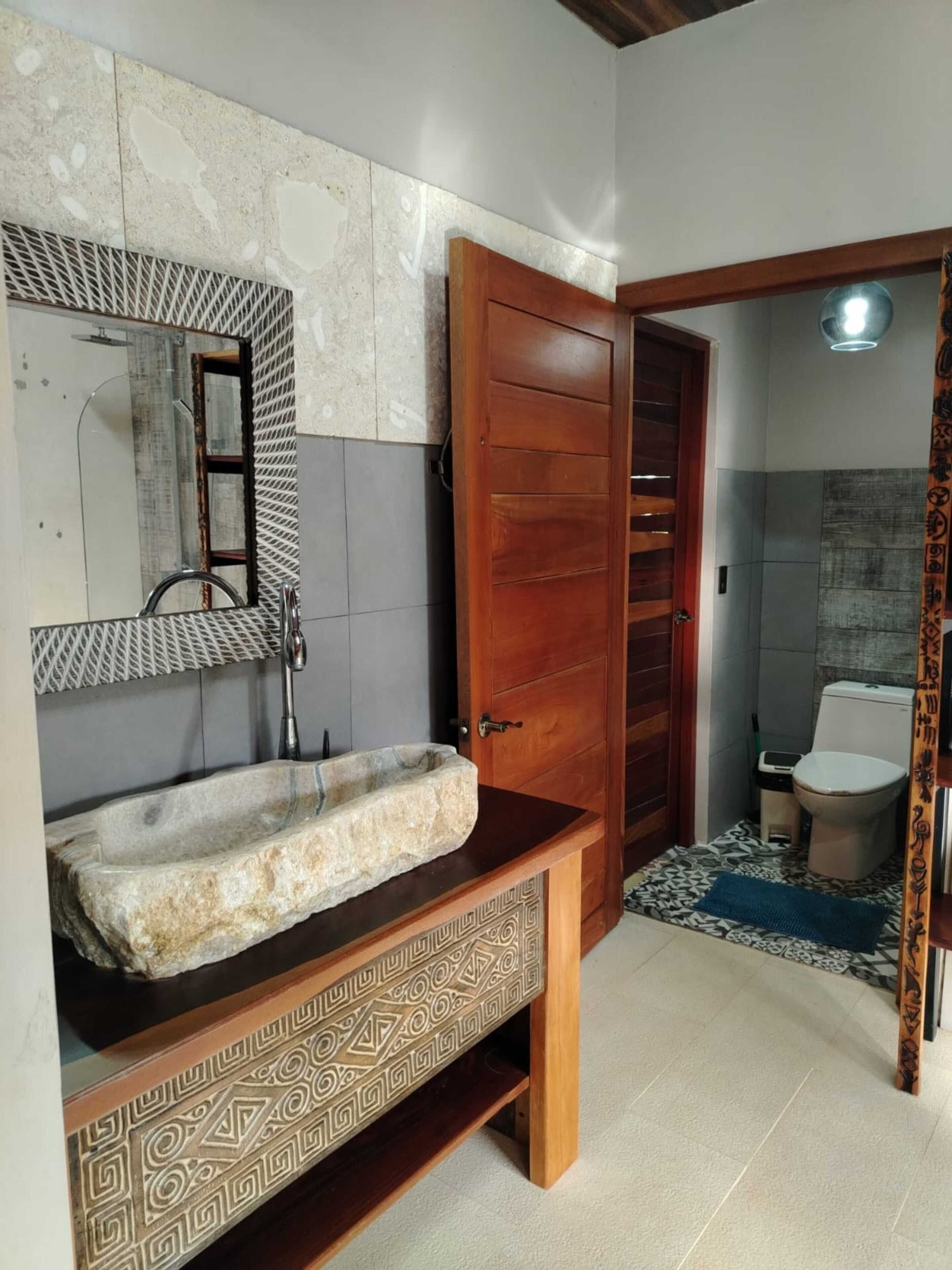A bathroom with a stone sink, wooden vanity, a mirror, and a shower area.