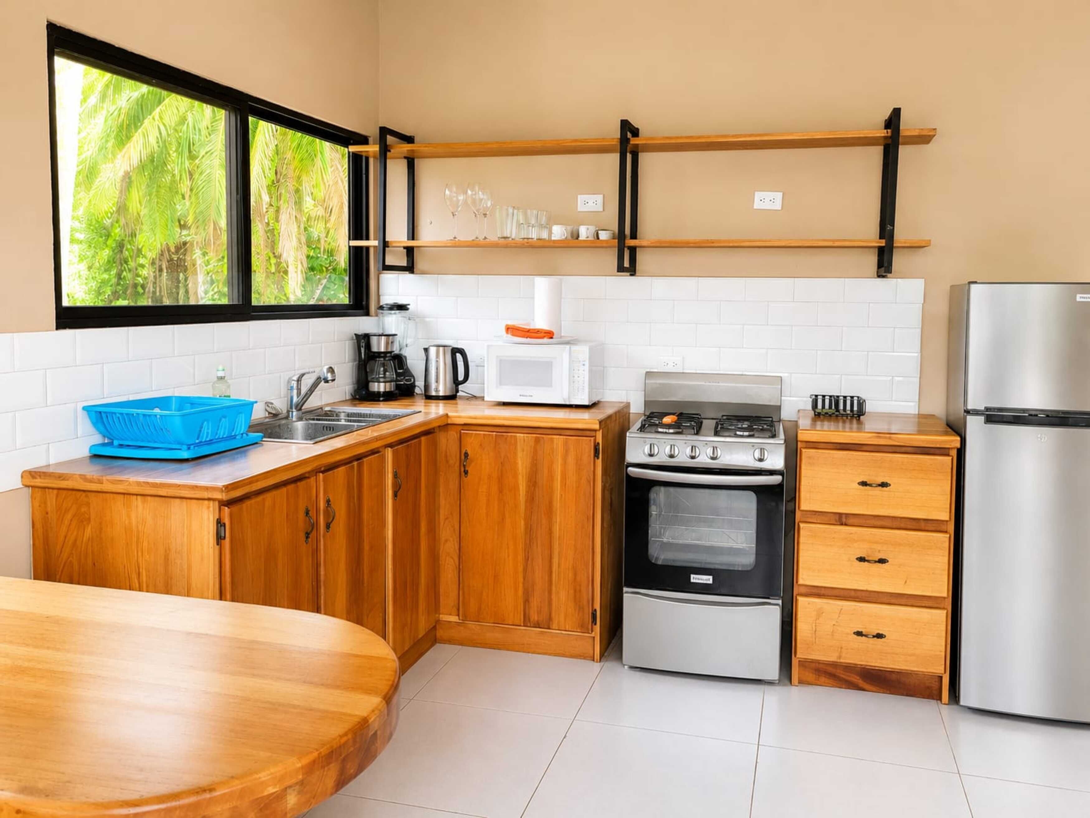 A kitchen with wooden cabinets, a gas stove, a microwave, a refrigerator, and a window with a view of greenery.