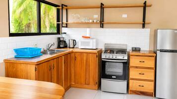 A kitchen with wooden cabinets, a gas stove, a microwave, a refrigerator, and a window with a view of greenery.