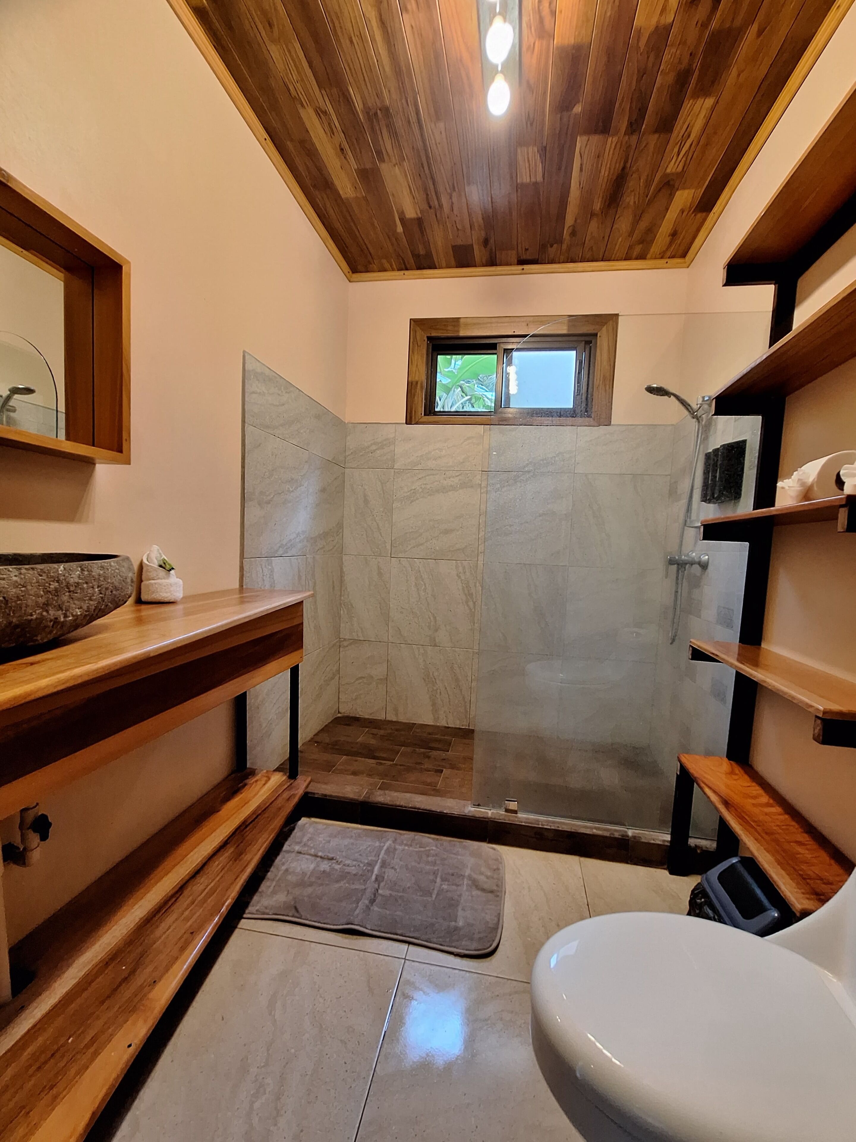 A bathroom with a wooden ceiling, a shower, a toilet, and a sink with a stone basin.