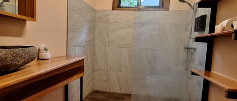 A bathroom with a wooden ceiling, a shower, a toilet, and a sink with a stone basin.