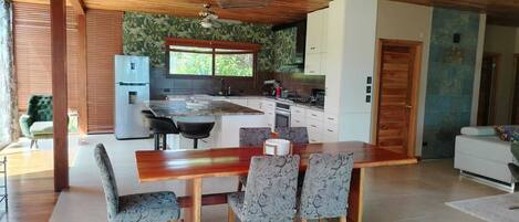 Una cocina moderna con comedor, techo de madera y un ventanal grande.