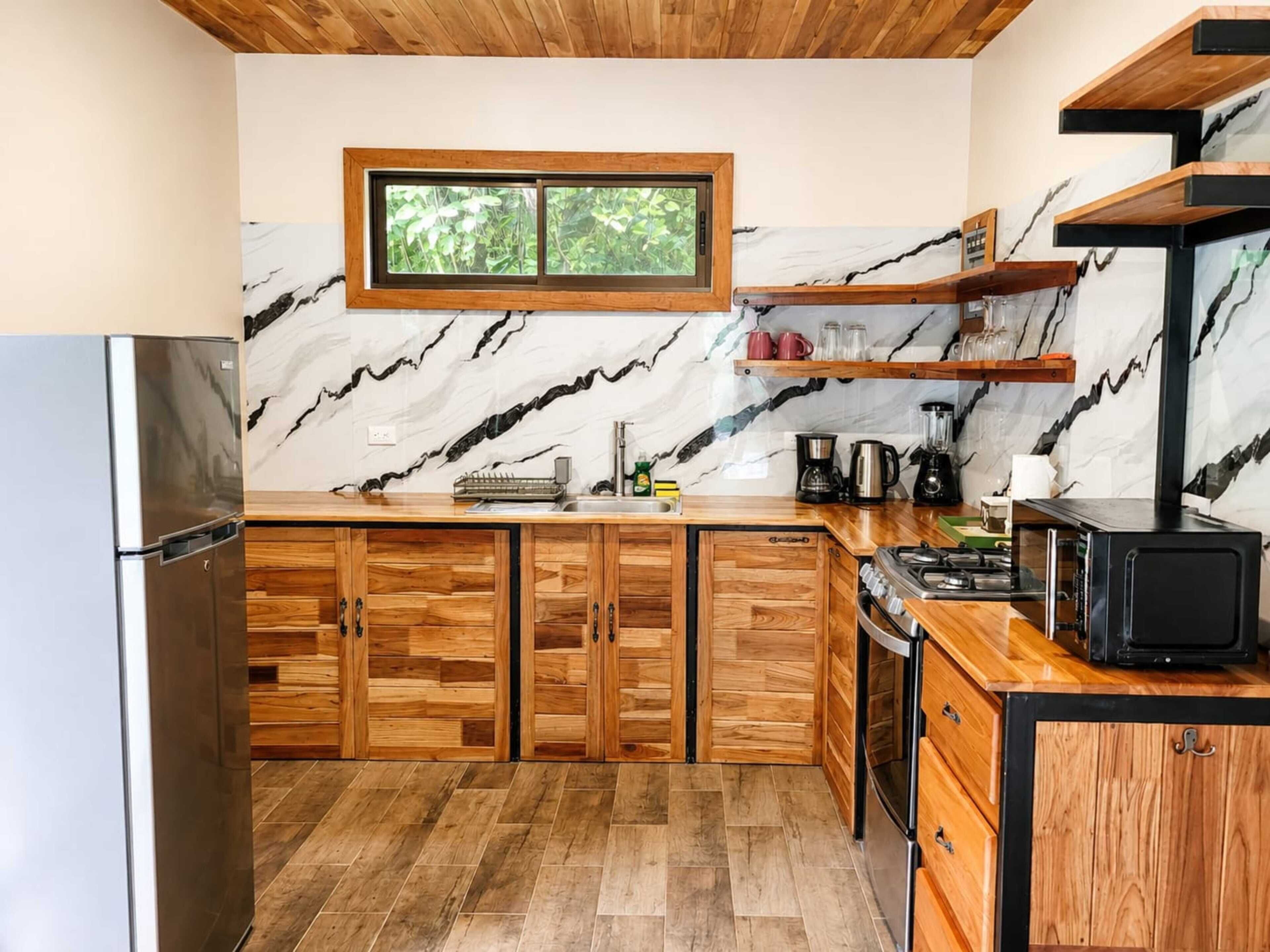 Cozinha com armários de madeira, painel de backsplash de mármore e janela com vista para vegetação.