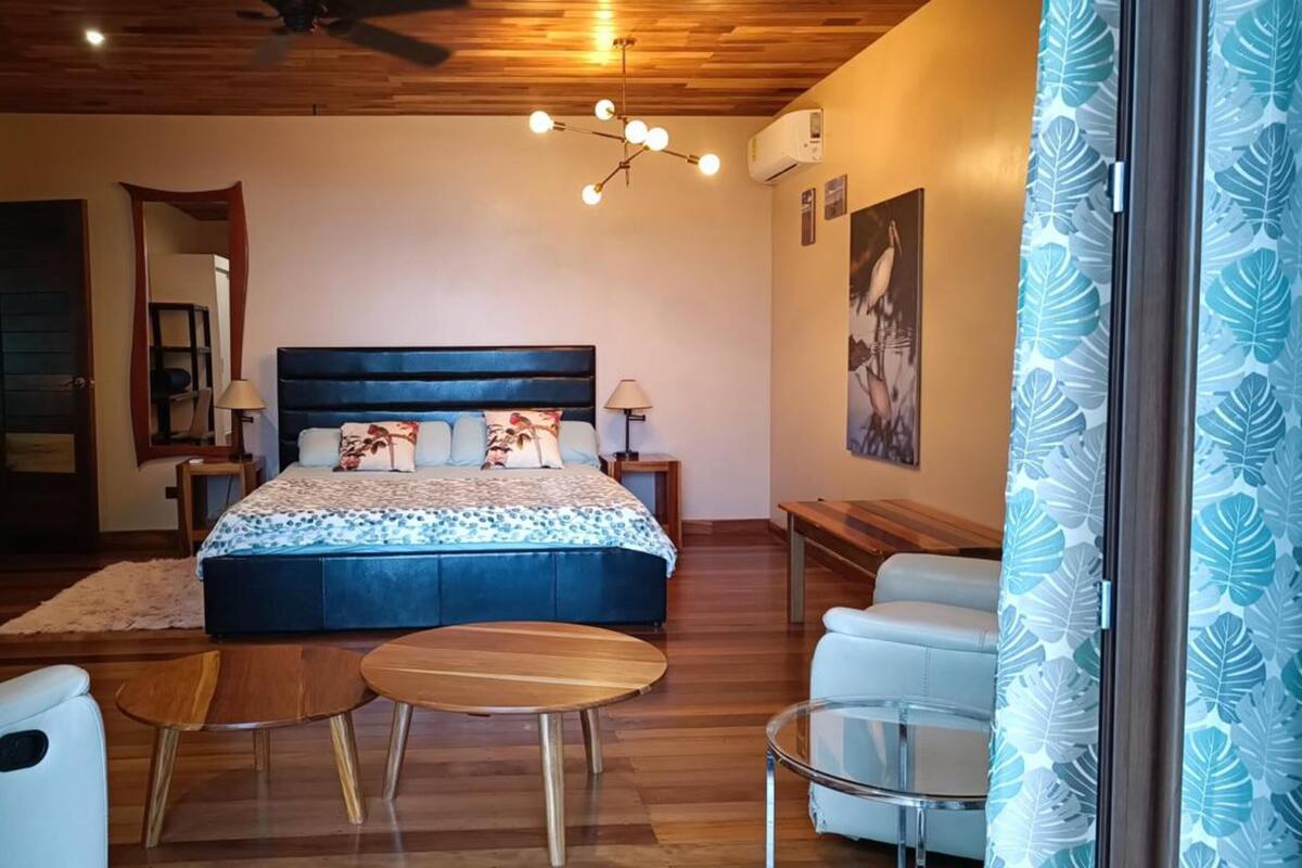 Een slaapkamer met een groot bed, twee nachtkastjes, een stoel, een ronde tafel en een plafondventilator.
