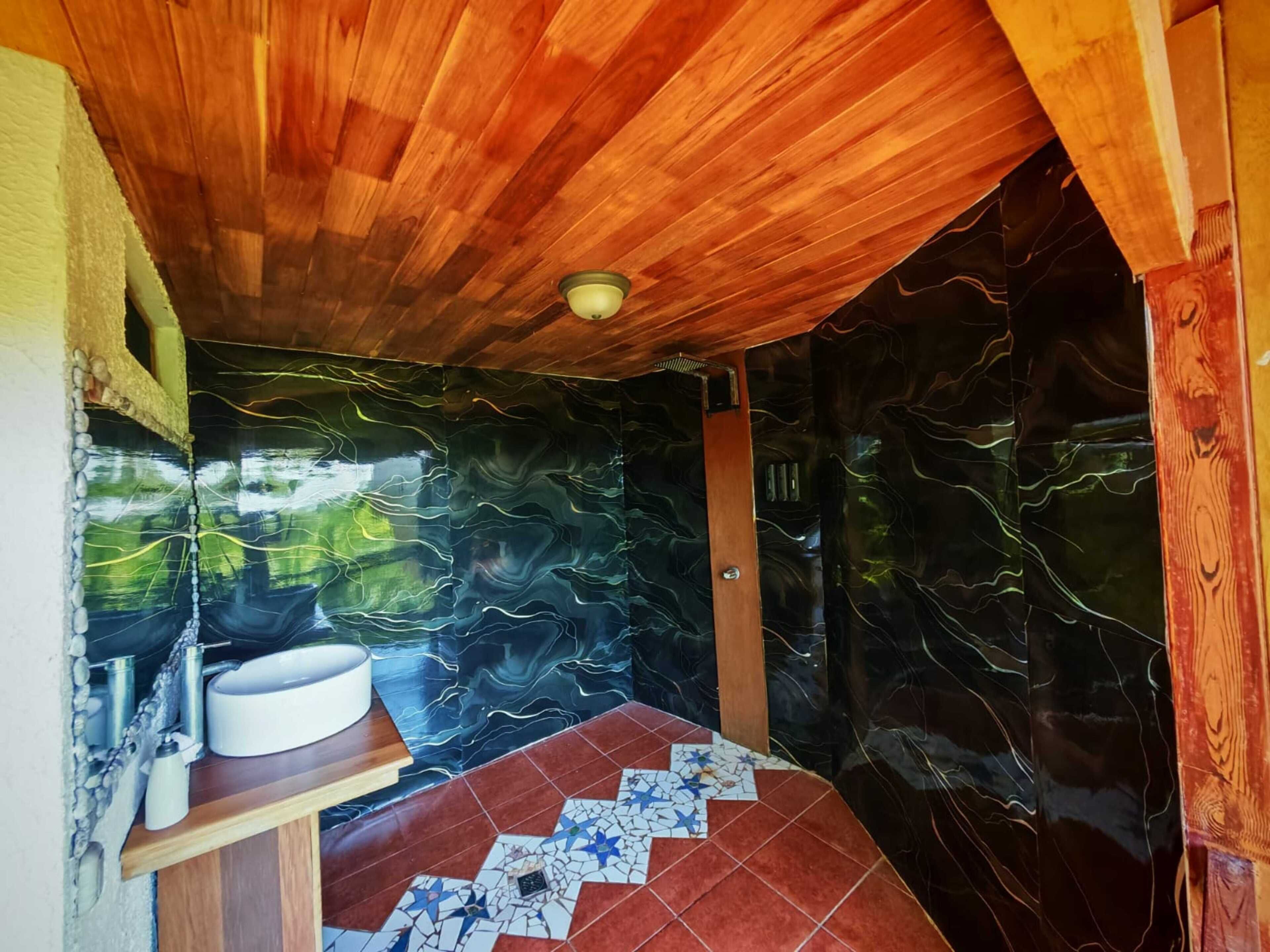 Une salle de bain avec un plafond en bois, un lavabo avec un bac blanc et un sol carrelé orné d’un motif en étoile.