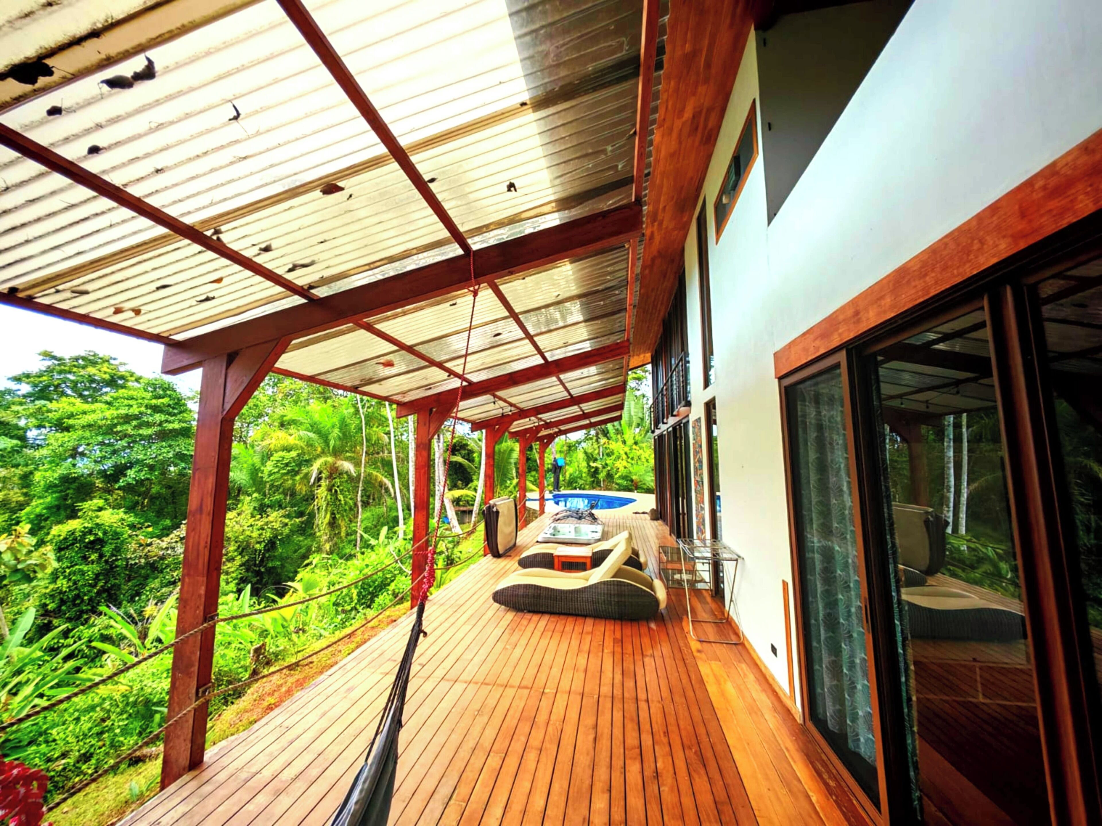 Um deck de madeira com uma rede, piscina e vegetação exuberante.