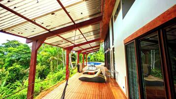 Um deck de madeira com uma rede, piscina e vegetação exuberante.