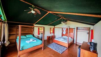 A room with two wooden beds, a ceiling fan, a small desk with a coffee maker, and a window with curtains.