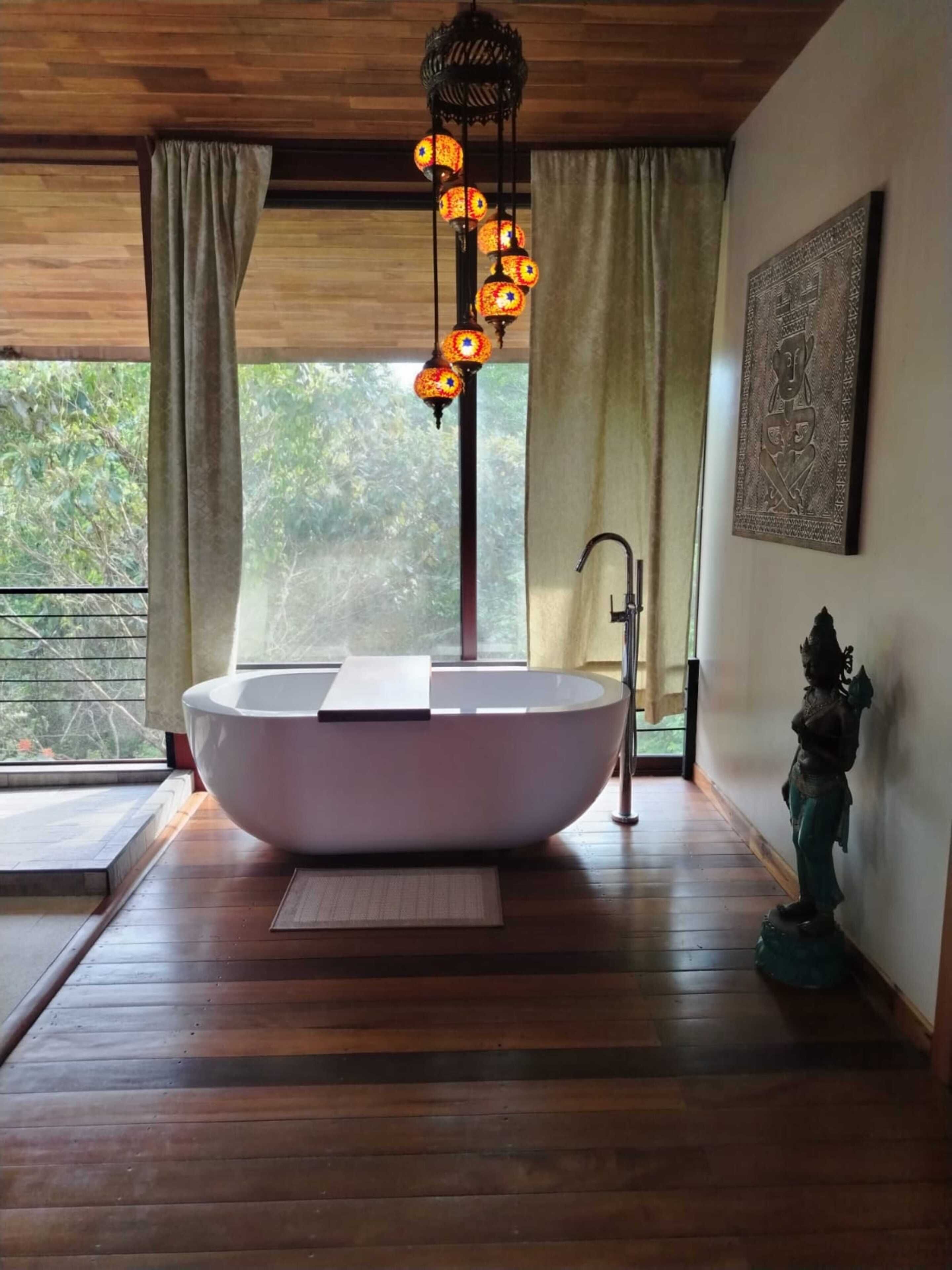 A modern bathroom with a freestanding bathtub, a hanging light fixture, and a statue on the wall.